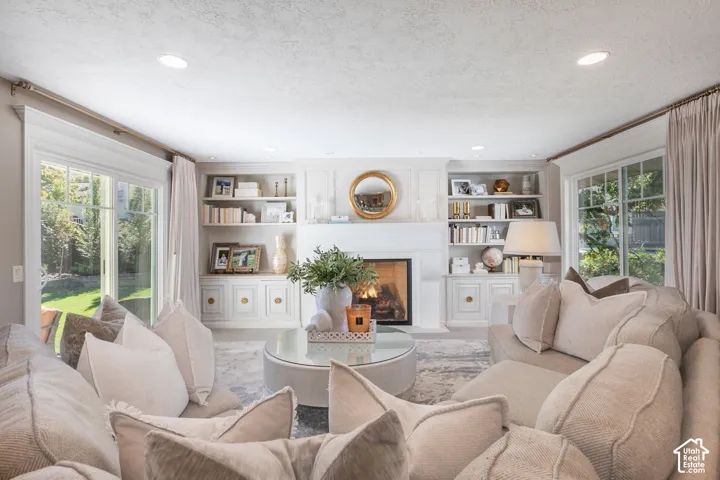 Elegant living room featuring built-in cabinetry with shelving and storage flanking a wood-burning fireplace, recessed ceiling lighting, and large multi-pane glass doors opening to outdoor space