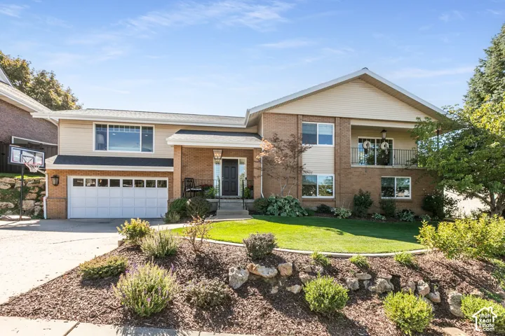 Brick and siding exterior with a two-car garage, front entry, upper balcony with iron railing, and manicured landscaping
