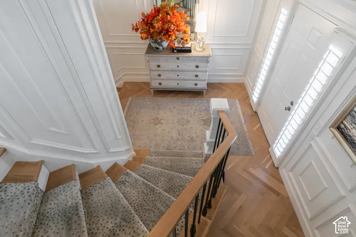 Elegant foyer featuring a curved staircase with wood railings and patterned carpet runner, hardwood flooring, white paneled doors, and a gray dresser with decorative floral arrangement