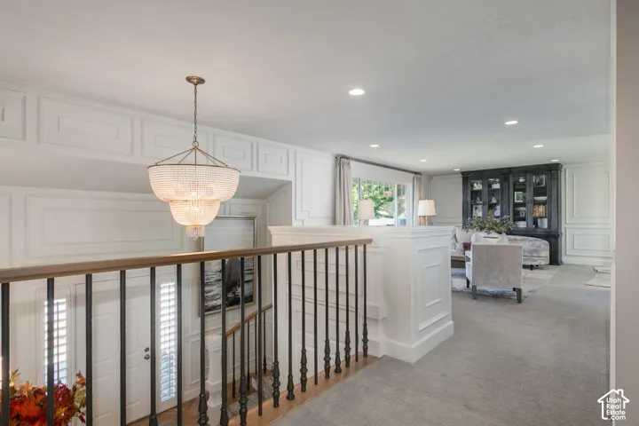 Tiered beaded chandelier, wainscoting, black iron spindle railing with wood handrail, recessed lighting, and a large window