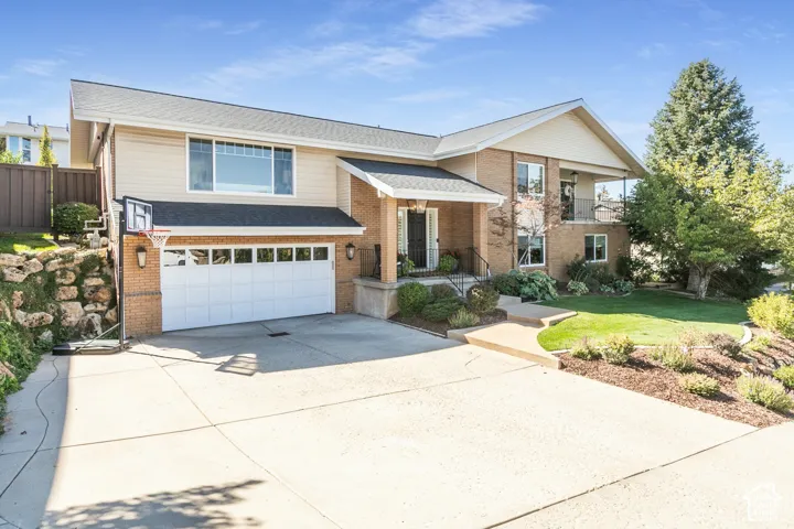 Brick and siding exterior with a multi-level design, attached garage, covered entryway, and mature landscaping