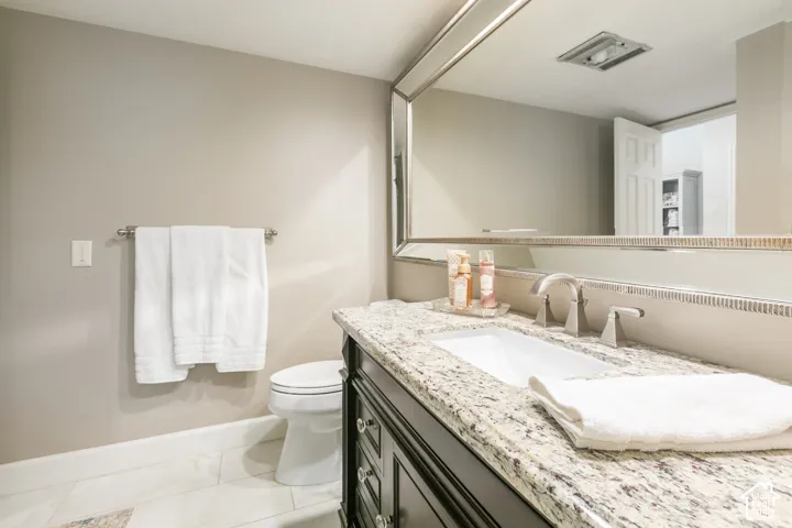 Vanity with integrated sink and chrome faucet, granite countertop, dark wood-finish cabinetry, and framed mirror