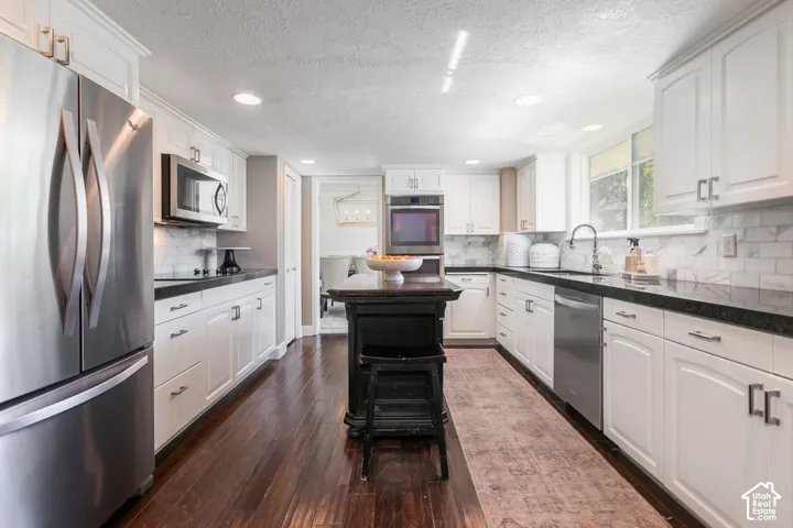Chef's kitchen featuring white shaker cabinetry, stainless steel French-door refrigerator and appliances, black granite countertops, subway tile backsplash, recessed and pendant lighting, and a large center island with dark wood-finish flooring throughout