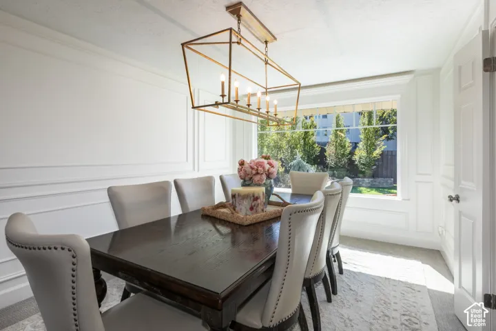 Elegant dining room showcasing a dark wood table, upholstered chairs with nailhead trim, geometric brass chandelier, wide-plank wood-finish flooring, and abundant natural light from large multi-pane windows with garden views