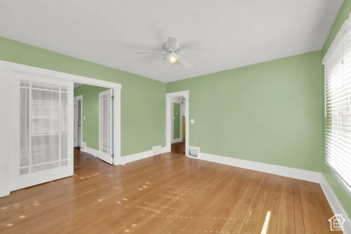 Wood-finish flooring, white trim, ceiling fan, and decorative glass panel doors