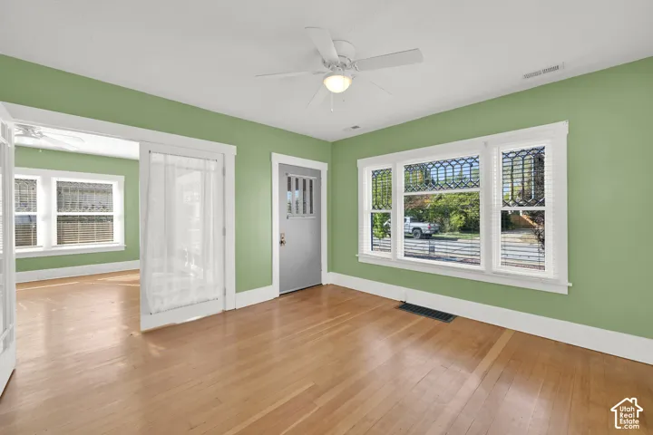 Hardwood-style flooring throughout, ceiling fan with integrated lighting, multiple windows with decorative grates, and a solid panel door with vertical lites