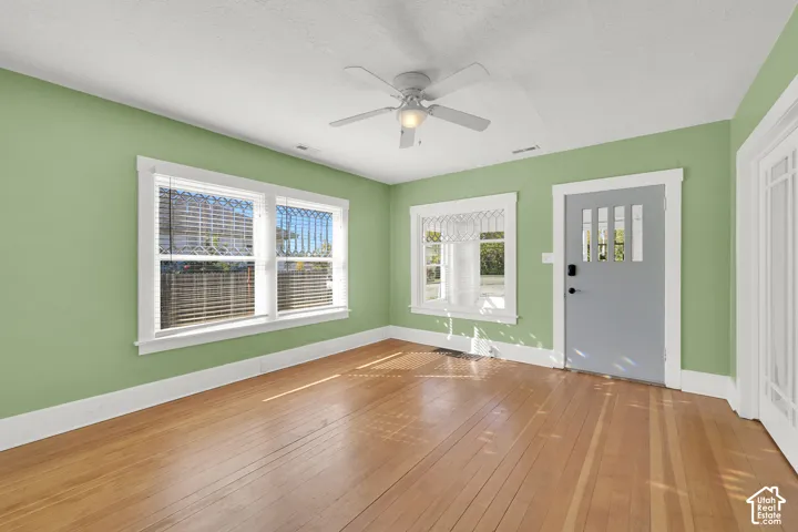 Wood-finish flooring, multiple windows, ceiling fan, and painted interior door