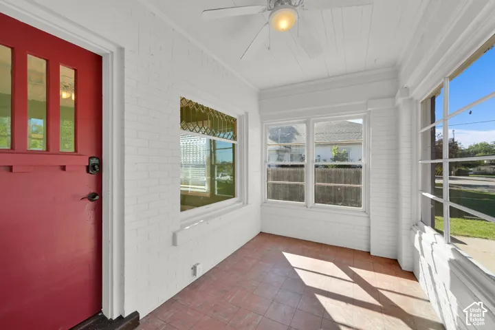 Enclosed porch featuring a red entry door with vertical lites, multiple windows, a ceiling fan with integrated lighting, and tile flooring