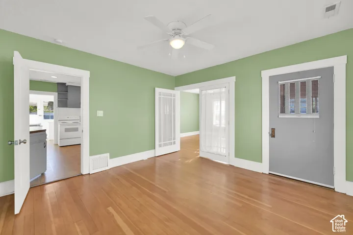 Hardwood flooring, ceiling fan, white trim, light green walls, and a view of the kitchen with white appliances