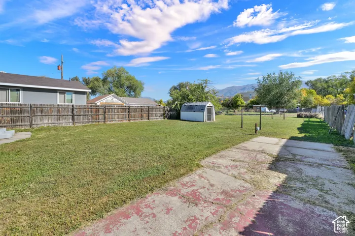 Expansive backyard with a green lawn, wood fence, concrete patio, and a utility shed