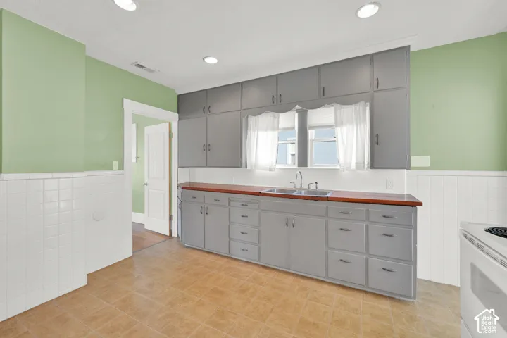Bright kitchen featuring custom gray cabinetry with ample storage, wood-finish countertops, and a stainless steel range