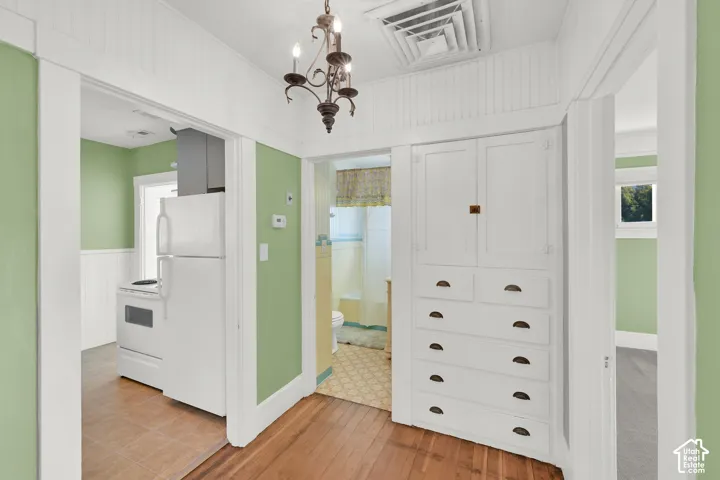 Wood-finish flooring, white beadboard wainscoting, built-in storage cabinetry with bronze hardware, and a bronze chandelier