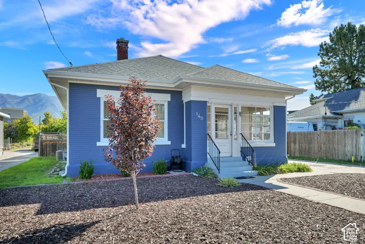 Charming blue cottage featuring a classic pitched roof, front-facing entrance with covered porch and steps, original brick chimney, and multi-pane windows