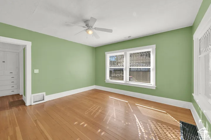 Wood-finish flooring, ceiling fan with integrated lighting, multiple windows with blinds, built-in cabinetry, and white trim
