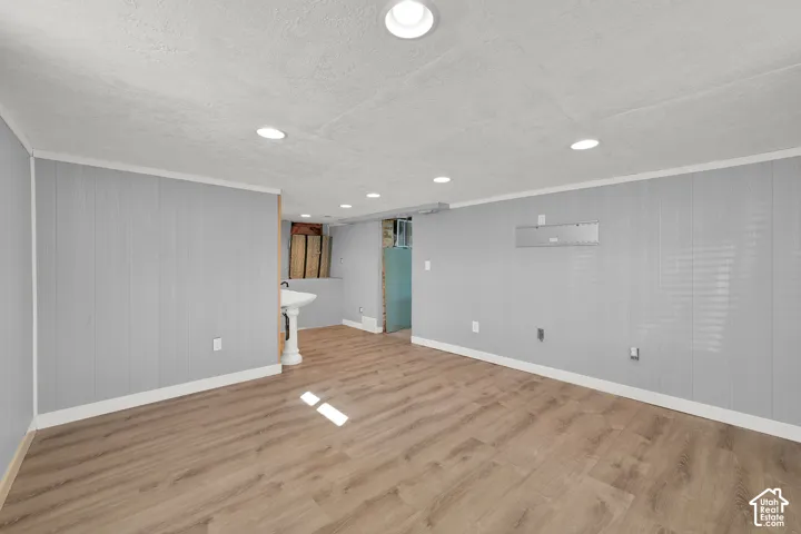 Recessed ceiling lighting, wood-finish flooring, light gray wall paneling, white trim, and a pedestal sink