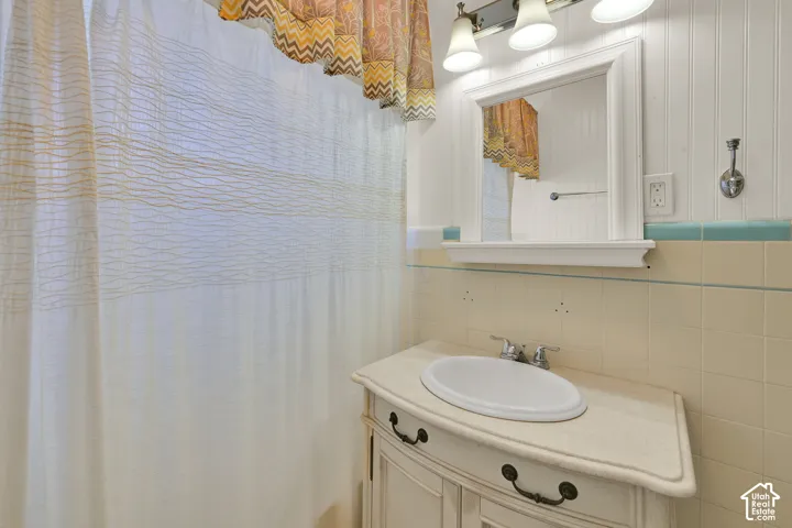White beadboard paneling, tiled walls with an aqua accent stripe, vanity with an integrated sink, framed mirror, and a three-light fixture