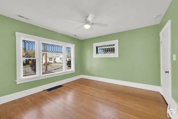 Hardwood-finish flooring, white baseboards, three-panel window with blinds, ceiling fan with integrated lighting, and a solid white door