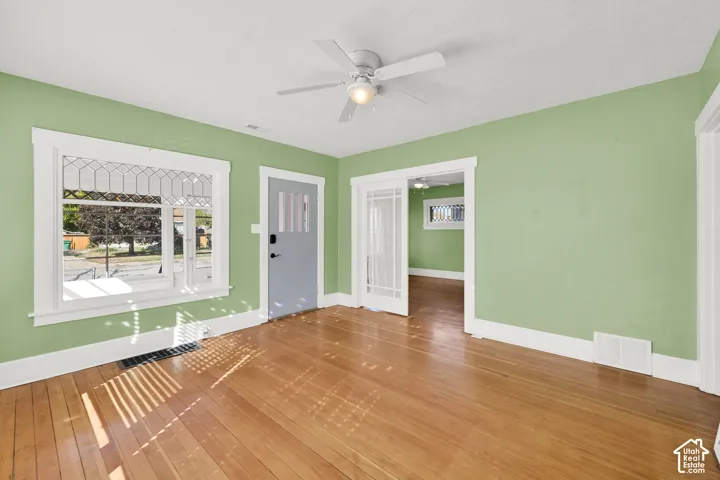 Wood-finish flooring, white ceiling fan with integrated lighting, white trim accents, and a front entry door with vertical window inserts