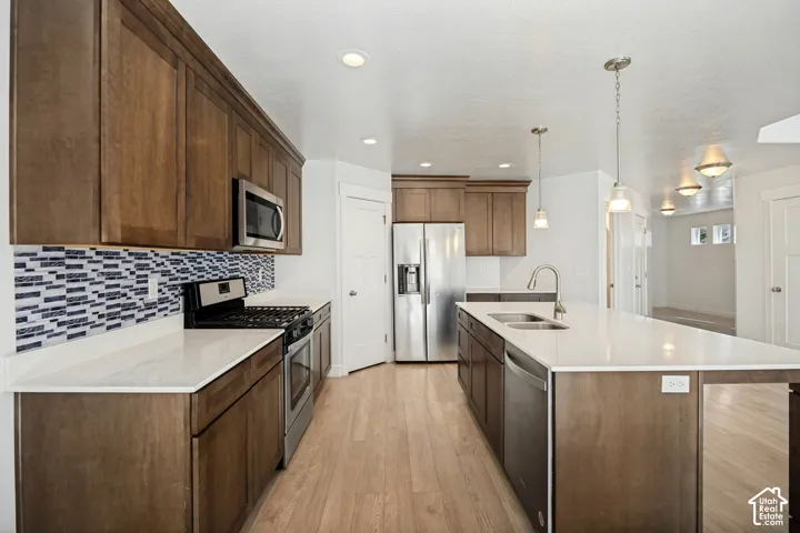 Kitchen featuring wood-finish cabinetry, stainless steel appliances, a mosaic tile backsplash, light-toned countertops, and wood-finish flooring