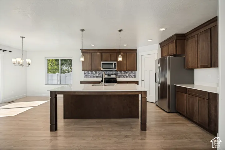Kitchen featuring wood-finish flooring, dark wood cabinetry, white countertops, stainless steel appliances, and a tiled backsplash