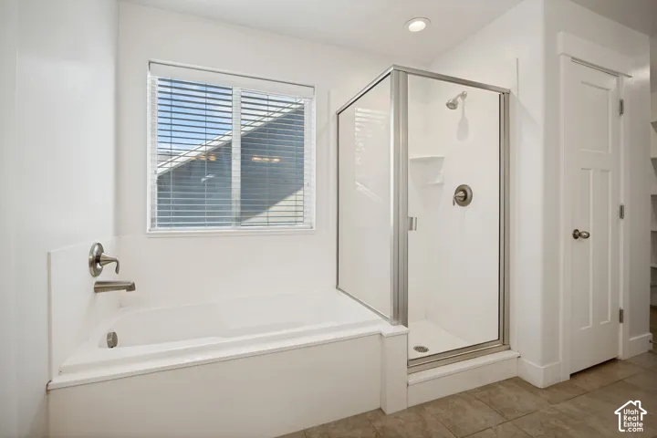 White built-in bathtub with brushed nickel fixtures, enclosed shower with glass door, and a single window with horizontal blinds