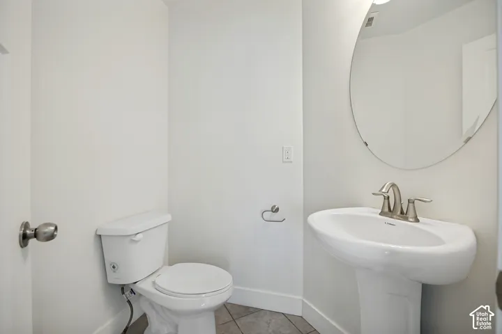 Pedestal sink with brushed nickel faucet, circular mirror, and tile flooring