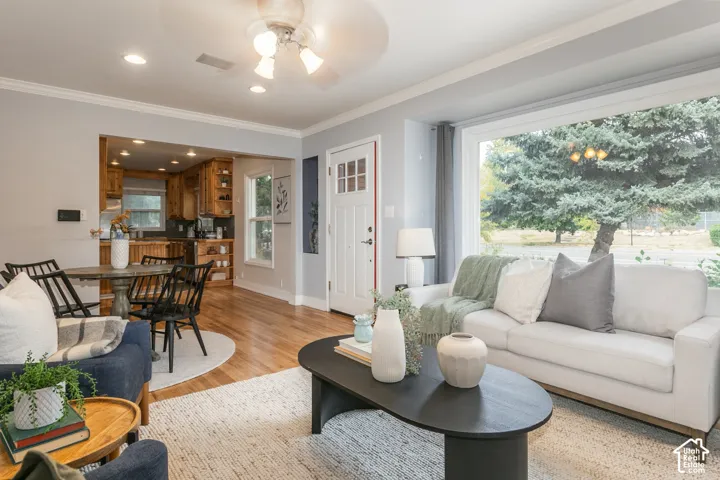 Hardwood flooring, crown molding, a ceiling fan with integrated lighting, a large picture window, and a white entry door with glass inserts