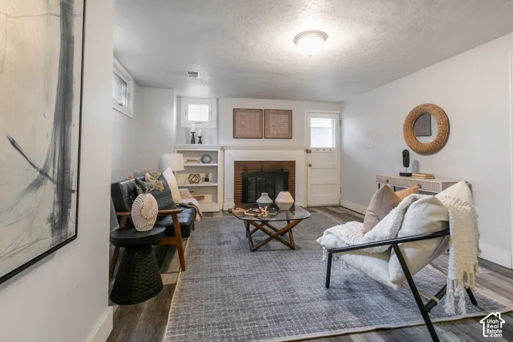 Living space featuring a brick fireplace with white mantel, built-in shelving, wood-finish flooring, and a flush-mount ceiling light fixture