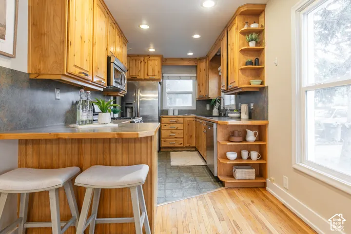 Wood-finish cabinetry with integrated open shelving, stainless steel appliances, solid surface countertops, and wood-finish flooring