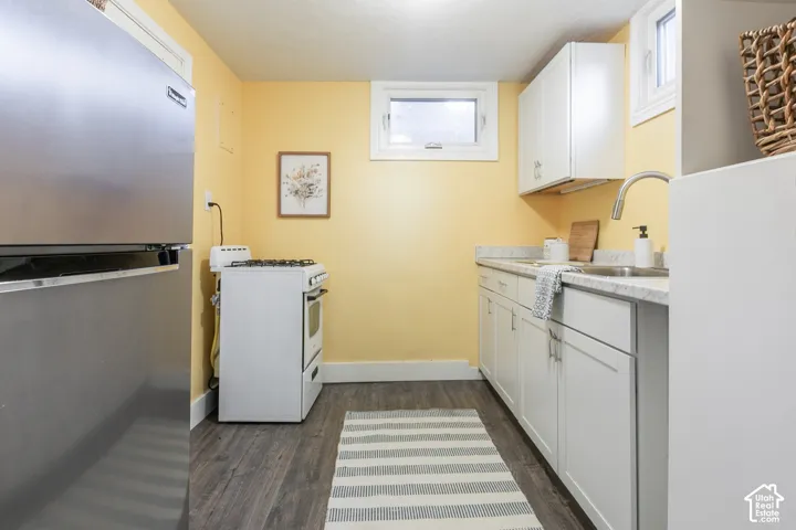 Wood-finish flooring, white cabinetry, stainless steel refrigerator, white range, and upper fixed windows