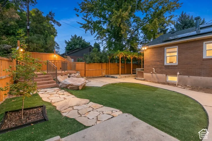 Fenced backyard featuring artificial turf, a stone pathway, an elevated wood deck with railings, and a wood pergola