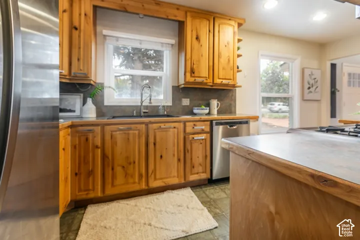 Custom wood cabinetry, stainless steel dishwasher, undermount sink with gooseneck faucet, window above the sink, and a stone-finish countertop