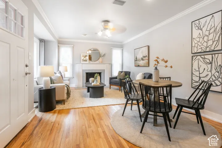 Hardwood flooring throughout, crown molding, a fireplace with a mantel, and a ceiling fan with integrated lighting