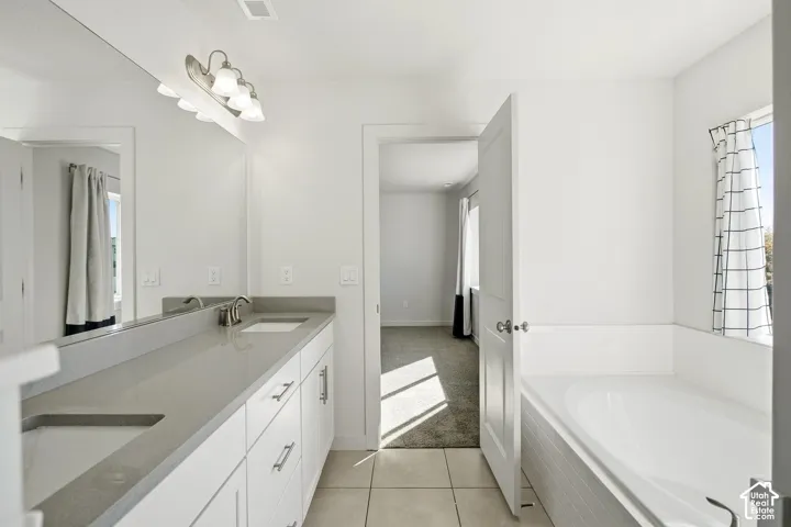Dual vanity with integrated sinks, ample countertop space, a large wall-mounted mirror, and a built-in tub