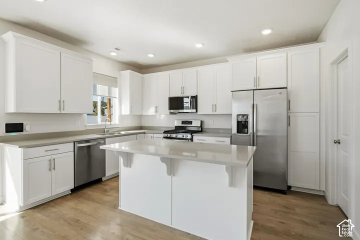 Bright kitchen featuring white shaker cabinetry, stainless steel appliances, a center island with counter seating, light-toned countertops, and wood-finish flooring