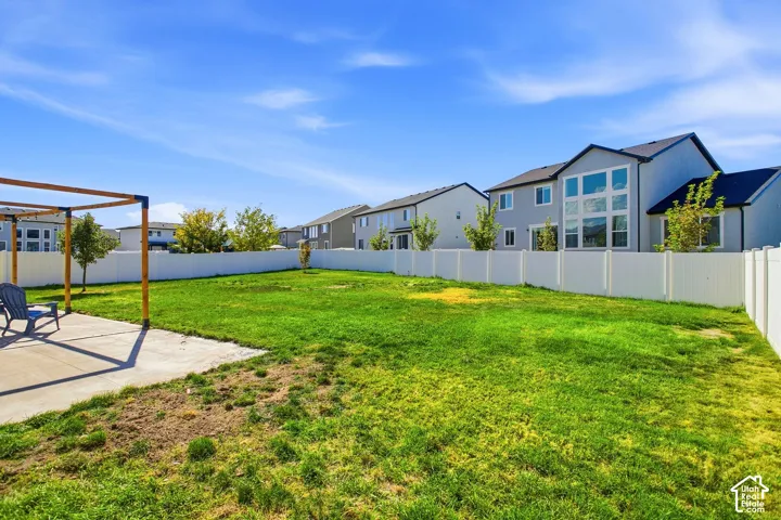 Expansive backyard featuring a lush lawn, white privacy fencing, concrete patio area, and a wood pergola