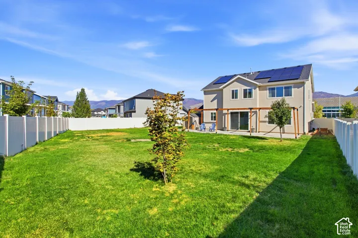 Expansive fenced backyard with a pergola, mature landscaping, and sliding glass door access to the residence