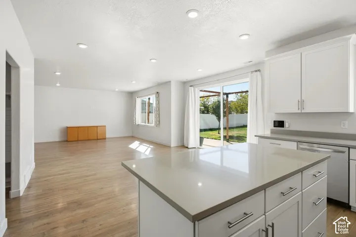 Kitchen island with a light-toned countertop, white cabinetry with silver-toned hardware, and recessed lighting
