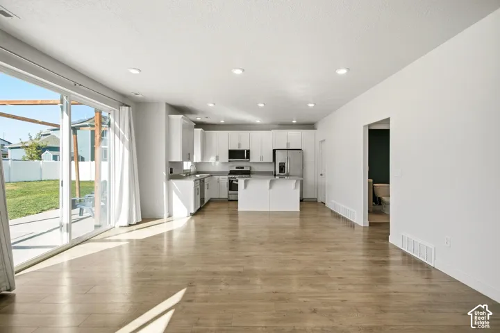 Open-concept kitchen with stainless steel appliances, white cabinetry, and gray countertops