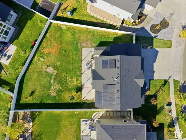Expansive backyard with a manicured lawn, white fencing, solar panels, and concrete driveway