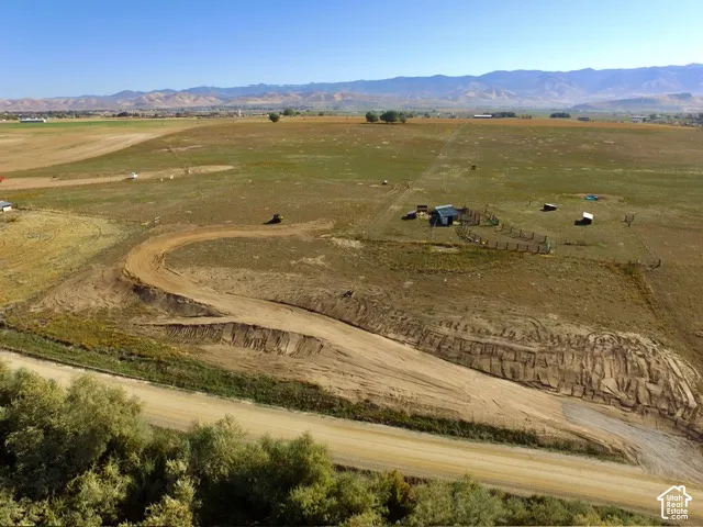 Expansive land parcel featuring a dirt track, partially fenced area, and distant mountain backdrop