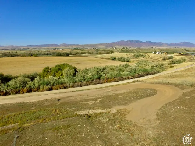 Expansive rural landscape featuring a dirt road, open fields, and distant mountains