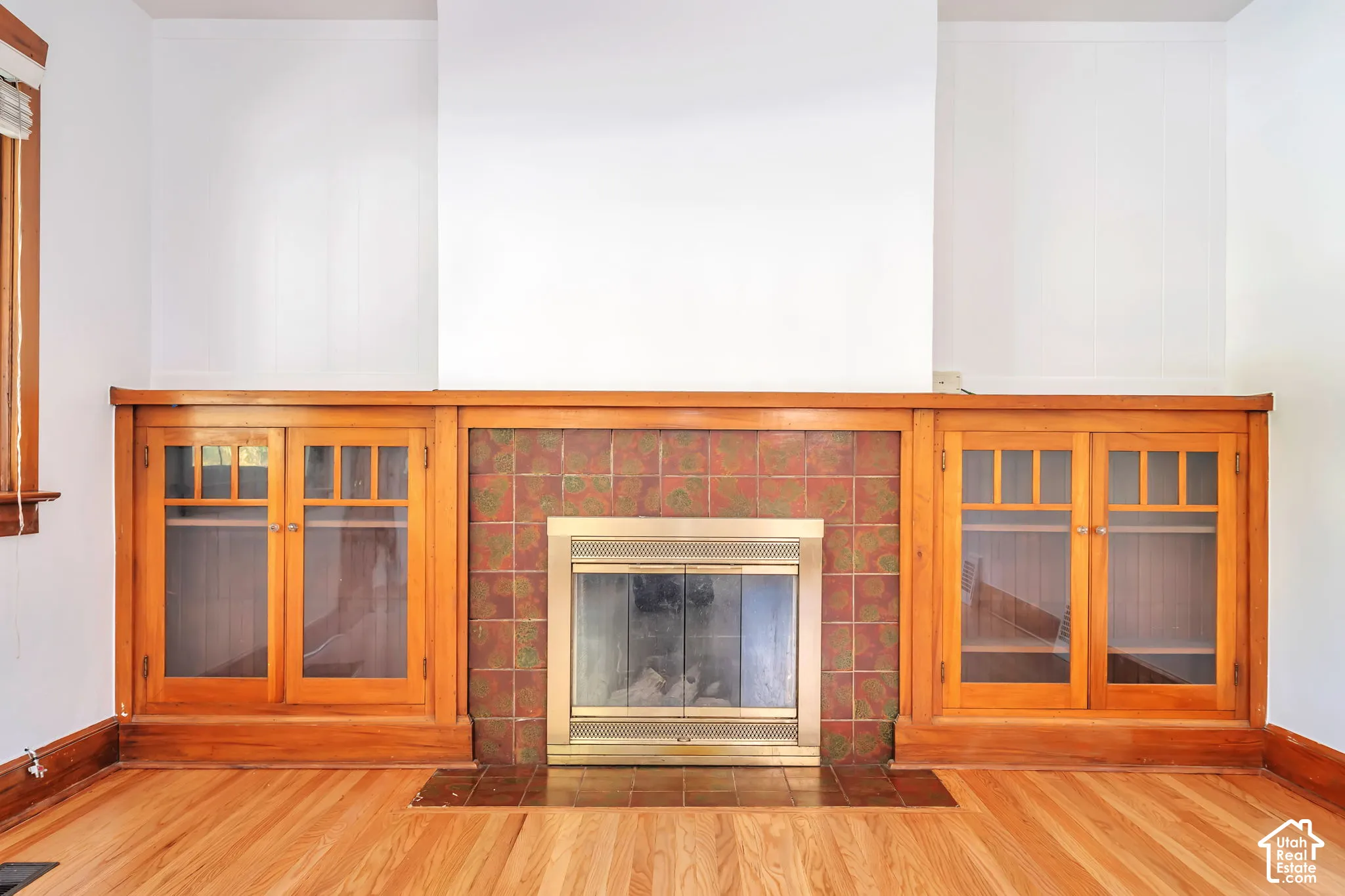 Built-in fireplace featuring a brass surround, brick-style tile, and gum wood-finish cabinetry with glass doors