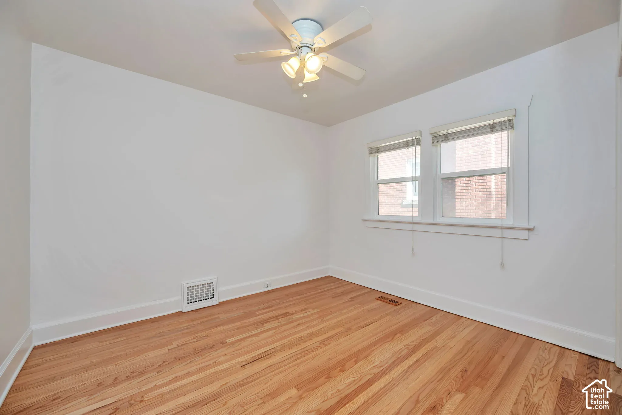 Upstairs bedroom with hardwood flooring, newly painted walls, white trim, dual windows, and ceiling fan with light fixture