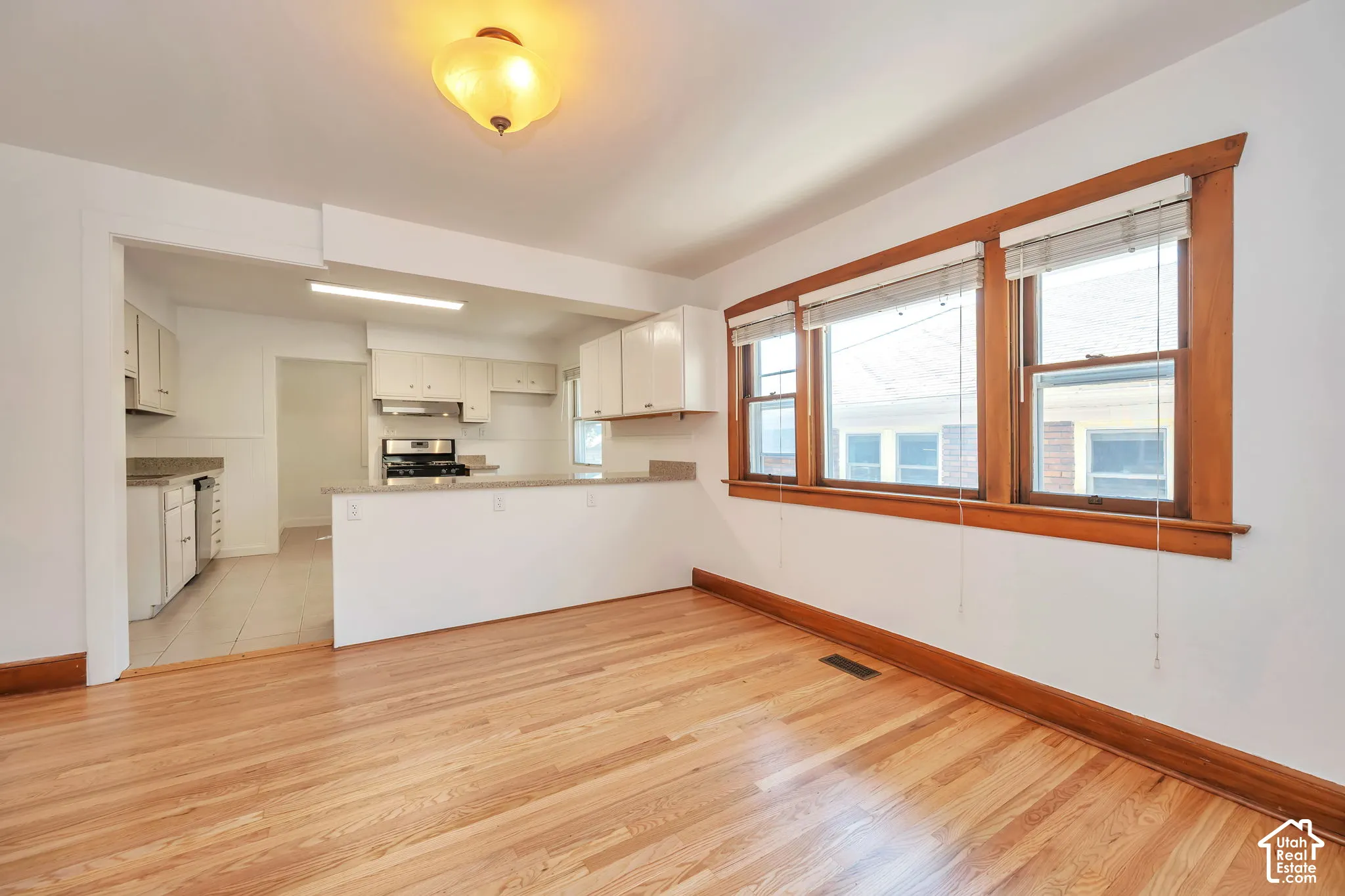 Hardwood flooring throughout, kitchen with white cabinetry and light-toned quartz countertops, stainless steel range and hood, and natural wood window trim