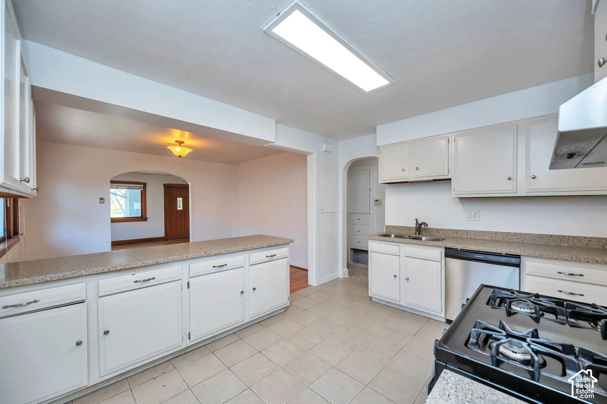 Kitchen featuring white cabinetry, light-toned quartz countertops, a stainless steel sink, and a black gas range