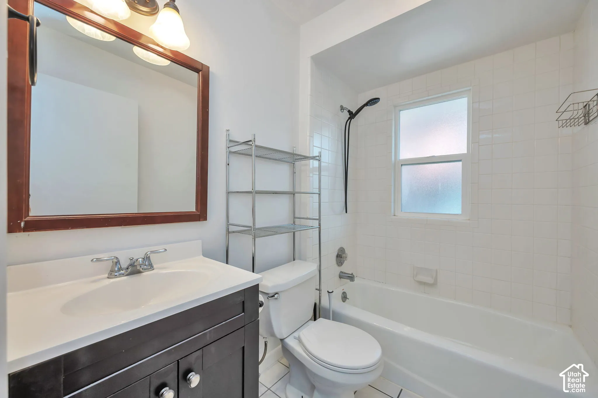 Upstairs main bathroom with tile flooring, dark wood-finish vanity with integrated sink, white tile shower surround, and a frosted window