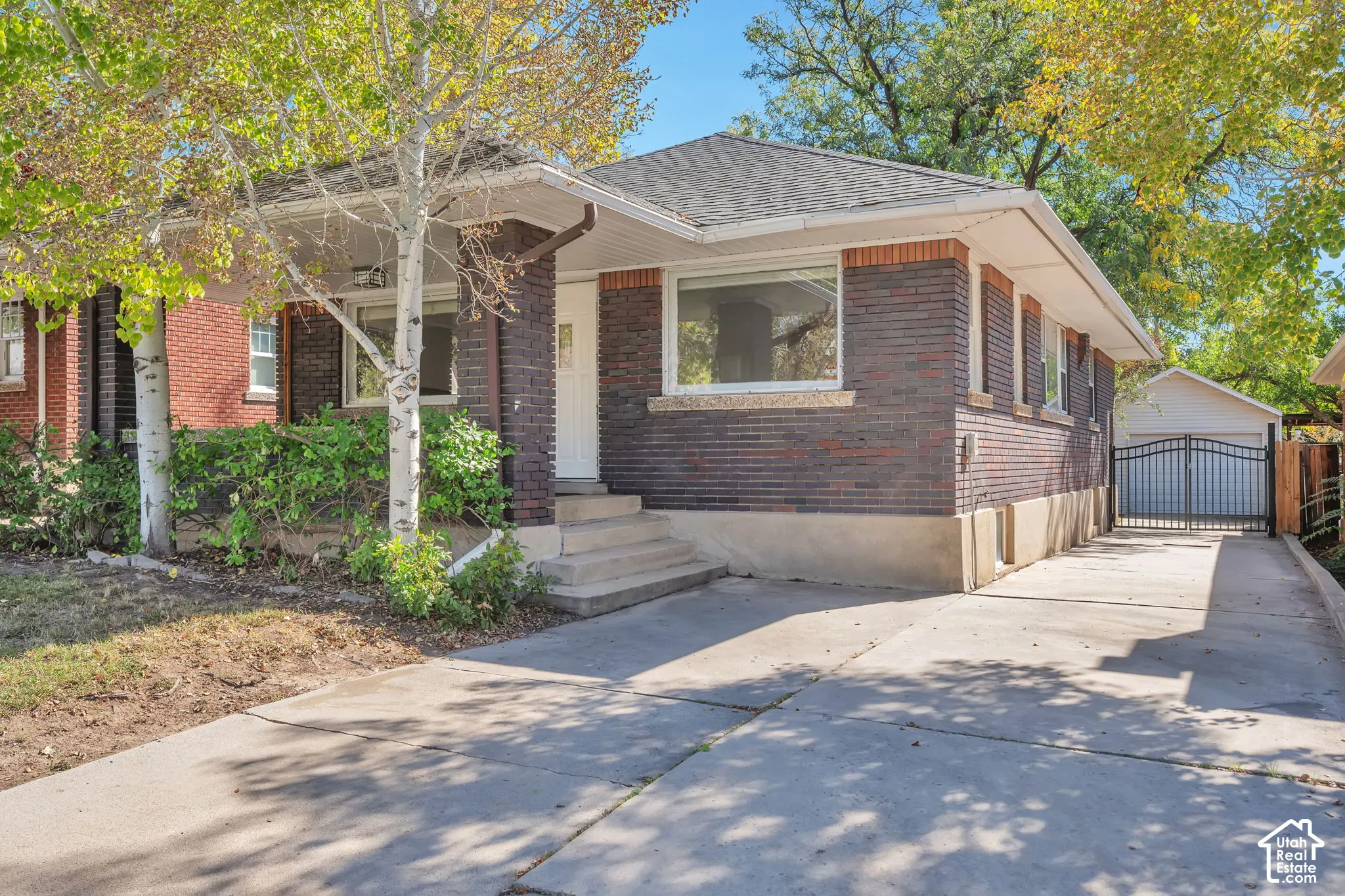 Brick exterior with stone accents, covered front porch, concrete driveway, and detached garage with privacy gate