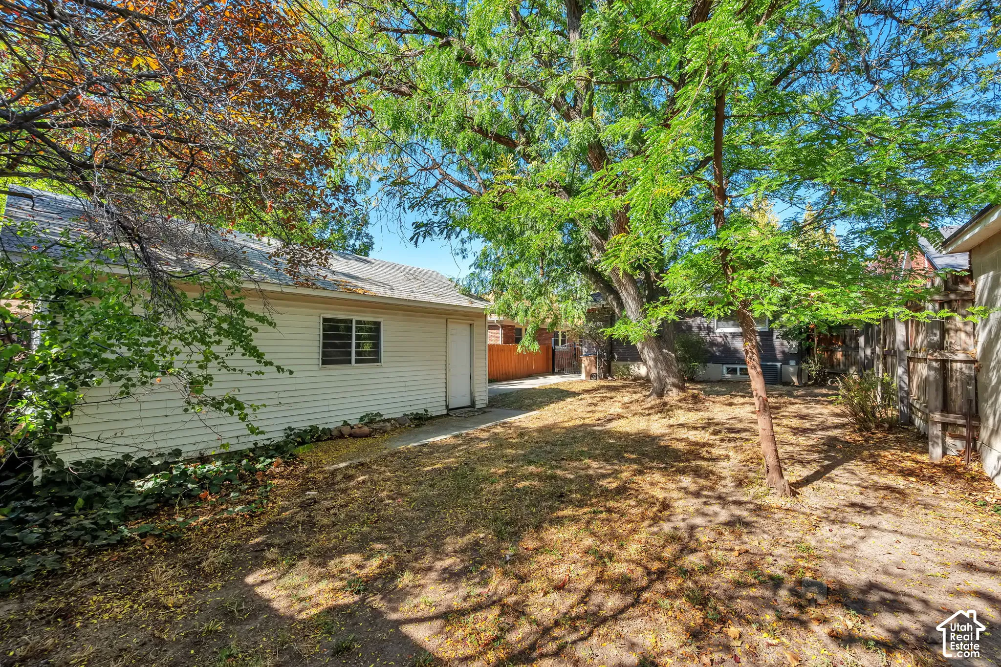 Detached garage with siding exterior and a side entry door, set within a yard featuring mature trees and wood fence