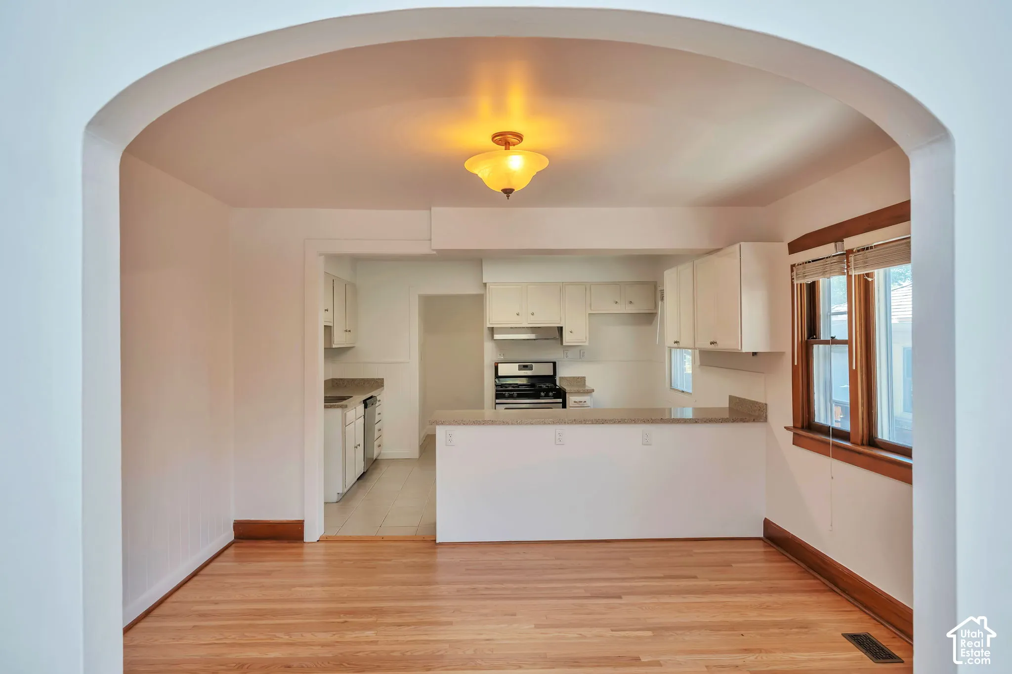 Hardwood flooring throughout, arched doorway, kitchen with white cabinetry, built-in breakfast bar, and wood-framed window